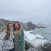 two girls wearing sweaters with arms around shoulders stand on a cliff in Big Sur Willow Creek smiling